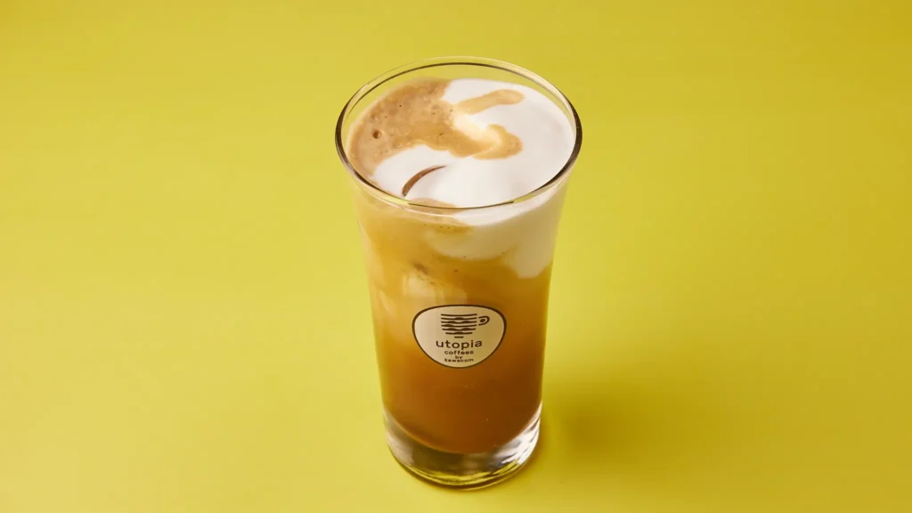 Freddo Cappuccino σε γυάλινο ποτήρι με πλούσιο αφρόγαλα, σε φόντο κίτρινο.